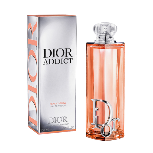 Dior Addict Peachy Glow Eau de Parfum bottle and packaging box on a white background. The rectangular bottle is filled with peach-colored liquid and features a silver Dior logo, while the box is metallic silver with peach accents and black text.