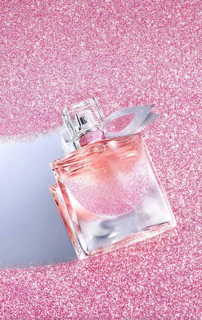 Pink perfume bottle with silver cap on a pink glittery background