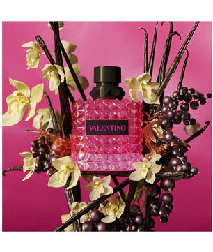 Pink perfume bottle with black cap surrounded by flowers and branches on a pink background