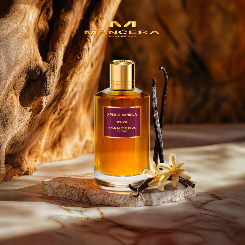 Mancera Xplific Vanilla perfume bottle with vanilla beans and flowers on a wooden surface.