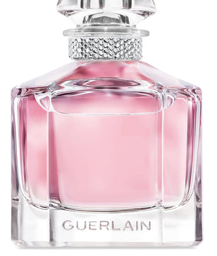 Guerlain perfume bottle with a faceted clear glass body filled with pink liquid, a silver rhinestone-embellished neck, and a clear sculptural cap on a white background.