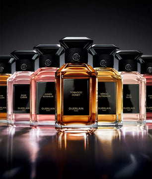 Collection of Guerlain perfume bottles on a reflective surface with a dark background