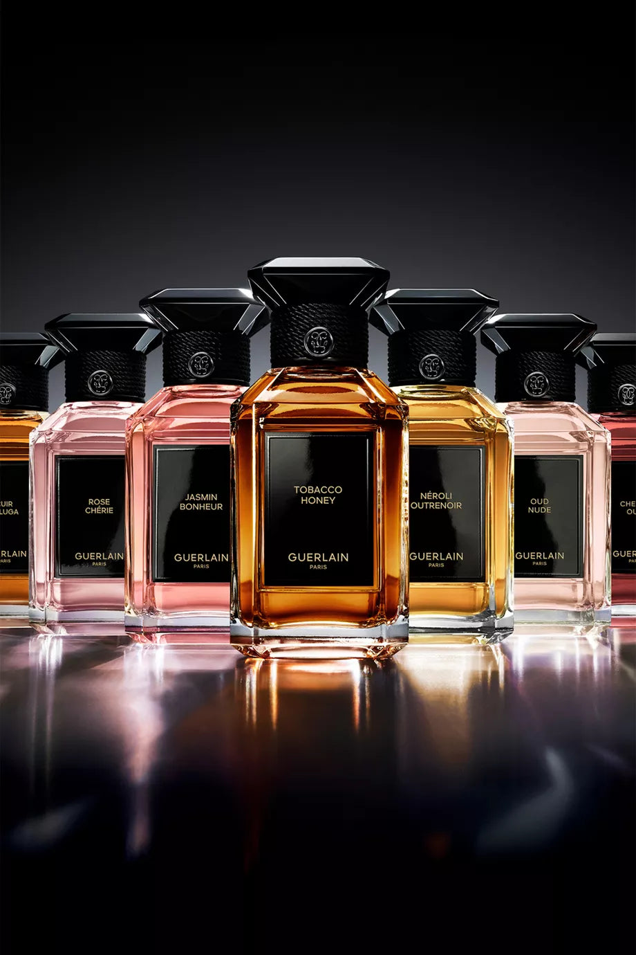 Collection of Guerlain perfume bottles on a reflective surface with a dark background