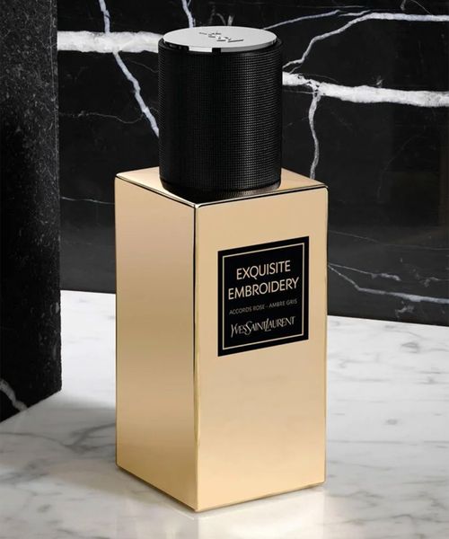 Gold perfume bottle with black cap on a marble surface against a dark marble background