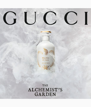 Gucci perfume bottle from 'The Alchemist's Garden' fragrance line, set against a smoky white and gray background with the brand name 'GUCCI' in large black letters at the top.