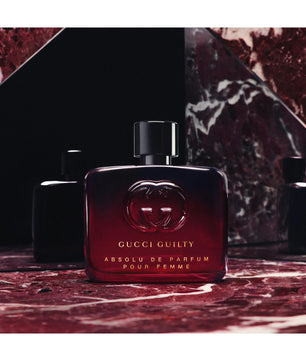 Gucci Guilty Absolu de Parfum Pour Femme perfume bottle in a dark red glass with gold lettering, displayed on a red marble surface with dark background.