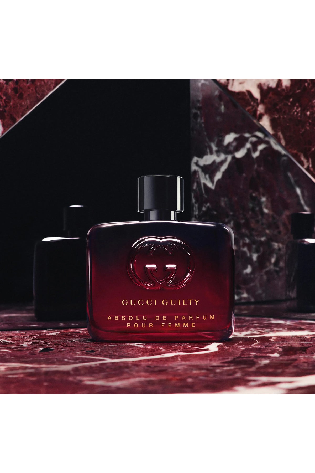 Gucci Guilty Absolu de Parfum Pour Femme perfume bottle in a dark red glass with gold lettering, displayed on a red marble surface with dark background.