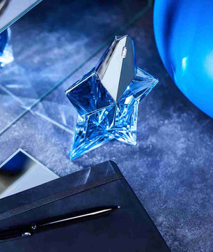 Blue star-shaped perfume bottle on a dark surface with a pen and notebook.