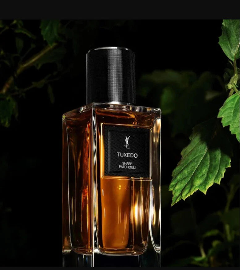 Perfume bottle labeled 'Tuxedo' with a dark background and green leaves.