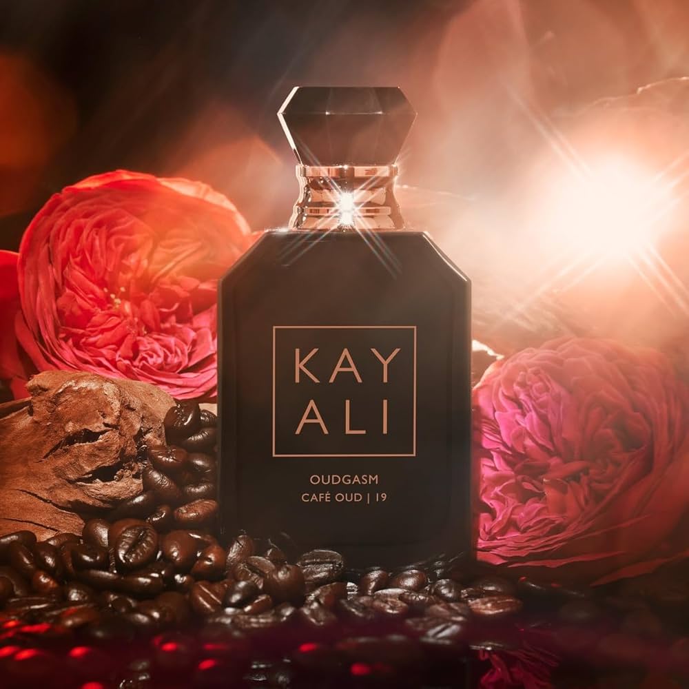 Perfume bottle labeled 'KAY ALI' surrounded by coffee beans and flowers on a dark background