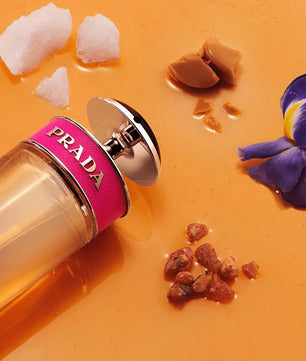 Prada perfume bottle with pink cap on an orange background with decorative elements
