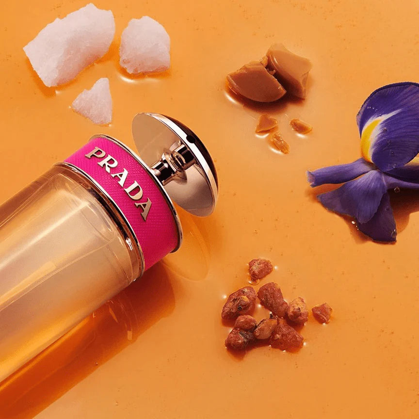 Prada perfume bottle with pink cap on an orange background with decorative elements