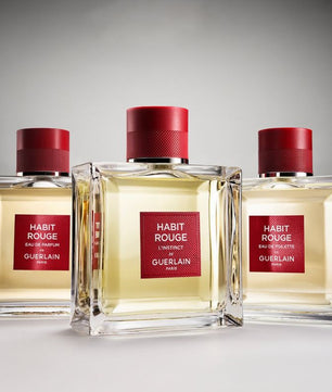 Three bottles of Habit Rouge perfume by Guerlain on a gray background