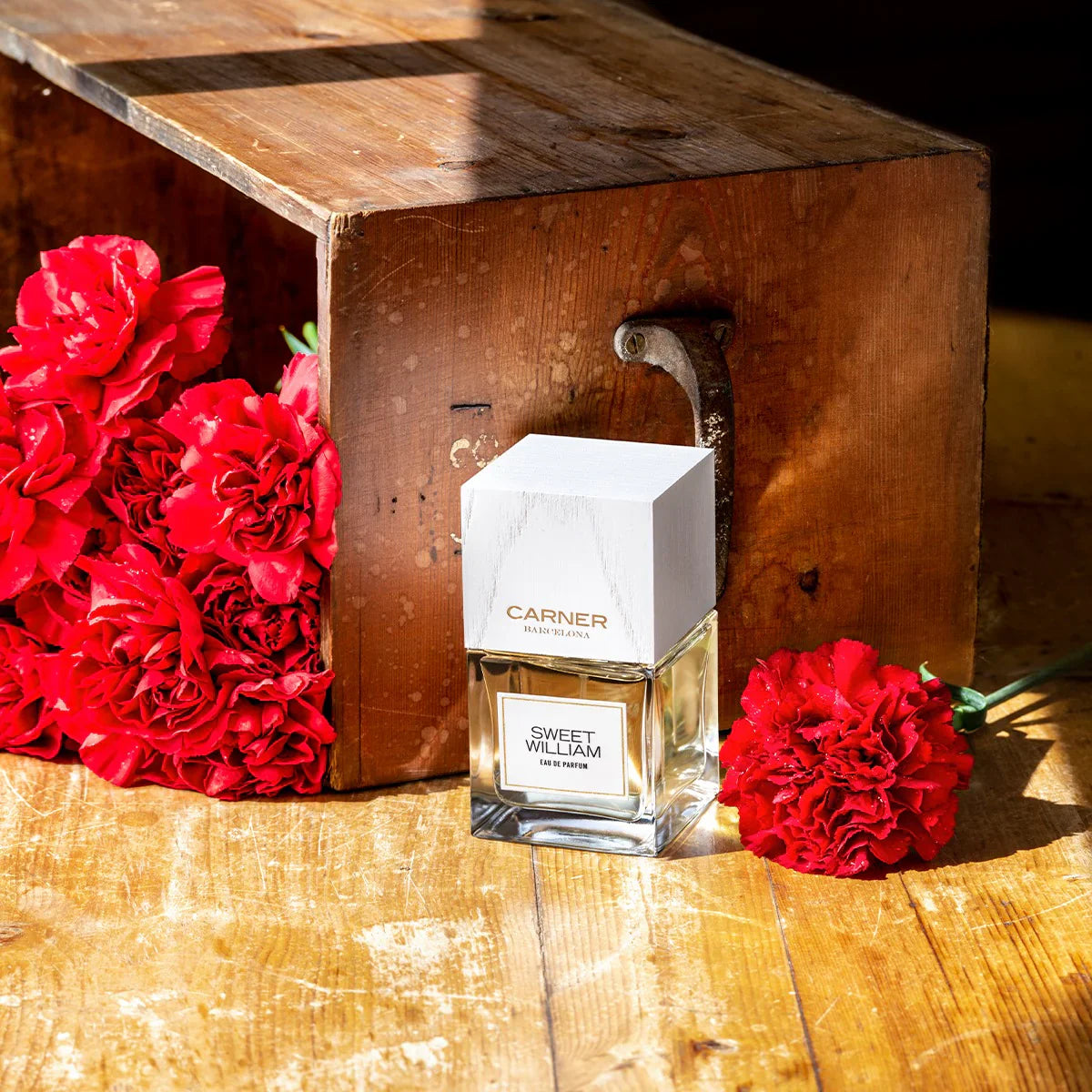 Carnier Sweet William perfume bottle with red flowers on a wooden surface