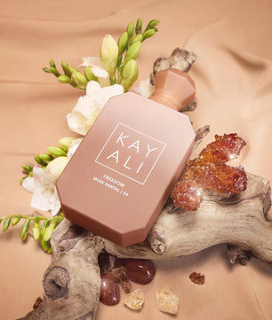 Kayali perfume bottle on a natural background with flowers and crystals