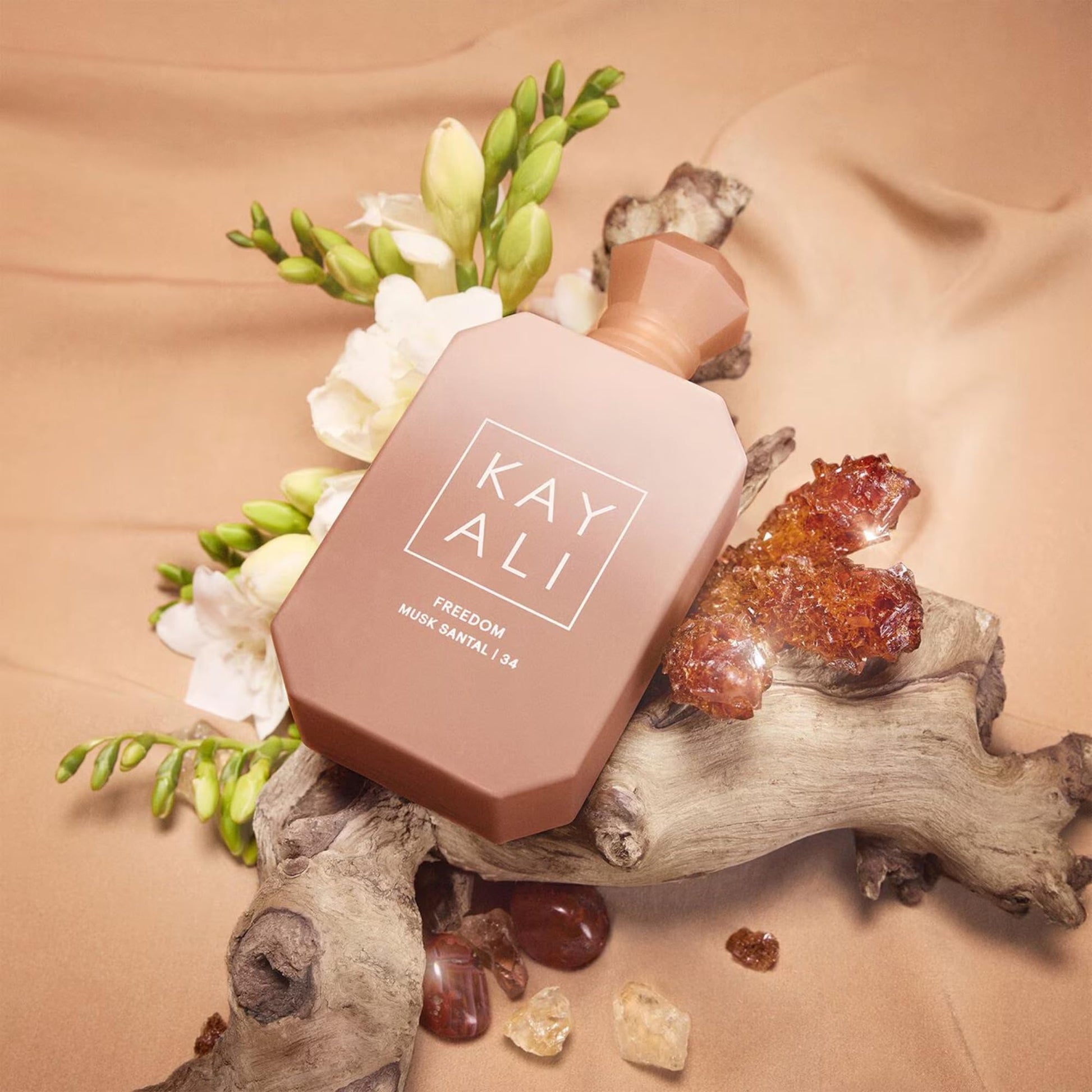 Kayali perfume bottle on a natural background with flowers and crystals