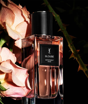 Perfume bottle with 'Yves Saint Laurent Blouse' label surrounded by pink roses on a dark background