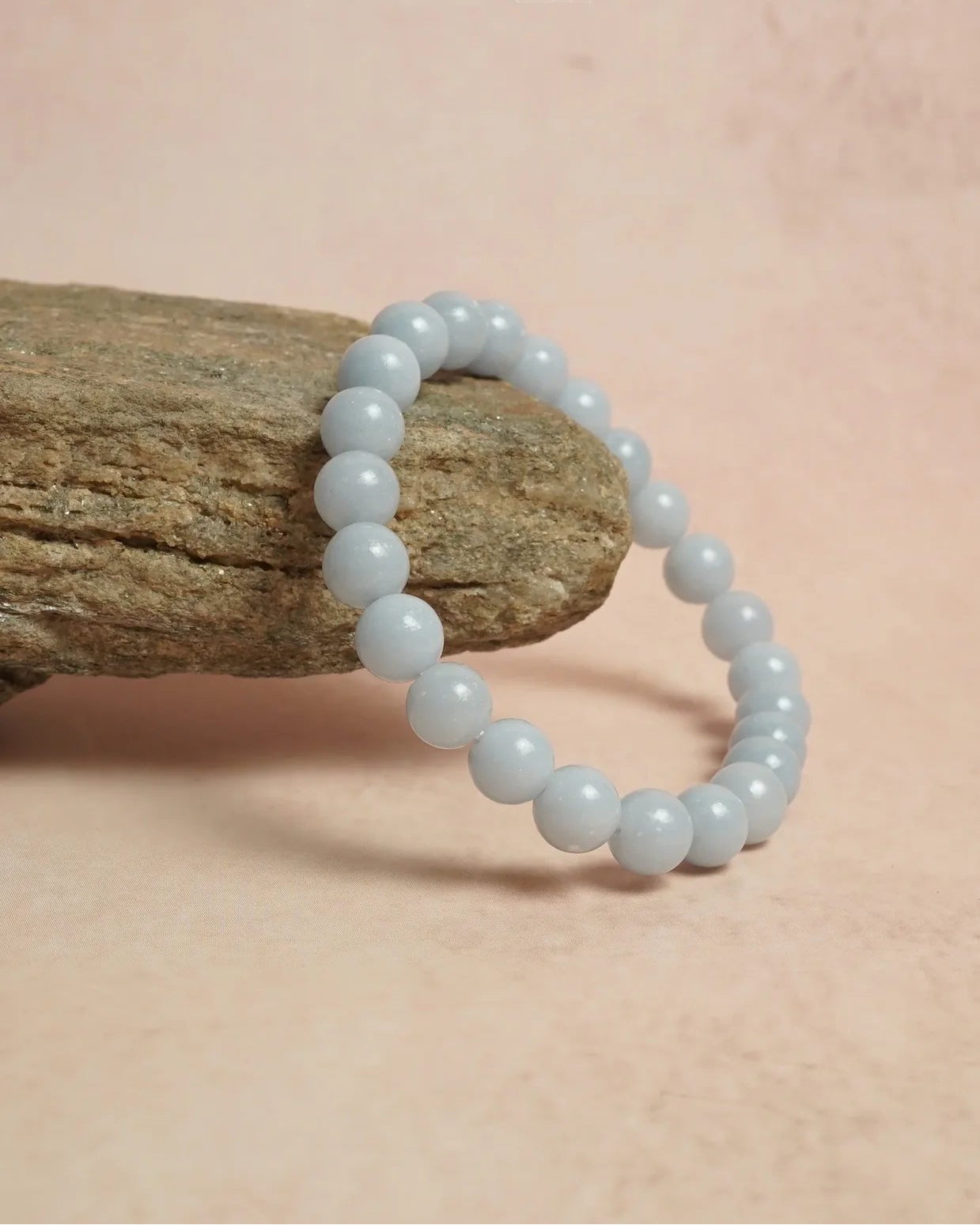 Light blue beaded bracelet on a stone with a soft pink background