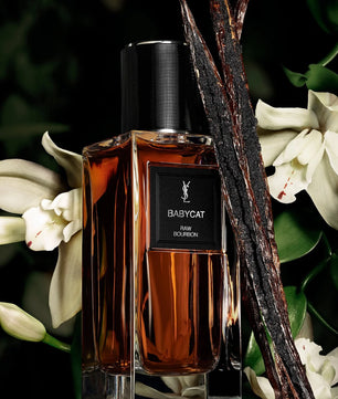 Perfume bottle labeled 'BABYCAT' with vanilla beans and flowers on a dark background