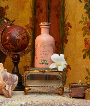 Decorative still life with a pink bottle, seashell, and globe against a floral wallpaper background.