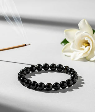 Black beaded bracelet on a white surface with a white flower and incense stick in the background