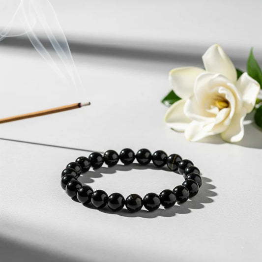 Black beaded bracelet on a white surface with a white flower and incense stick in the background