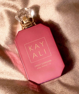 Pink perfume bottle with 'KAY ALI' branding on a beige fabric background