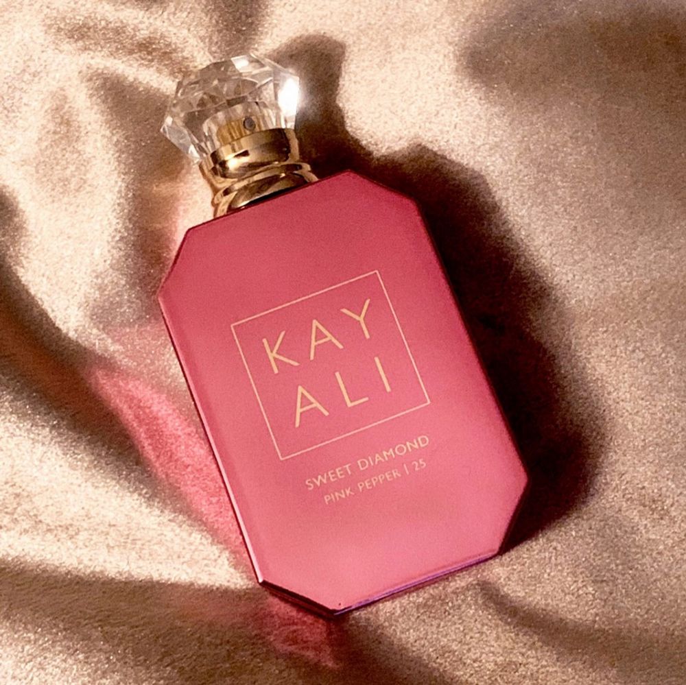 Pink perfume bottle with 'KAY ALI' branding on a beige fabric background