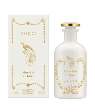 Gucci Muschio di Luce Eau de Parfum shown with its white box and frosted glass bottle, both decorated with gold foil detailing and a peacock illustration.