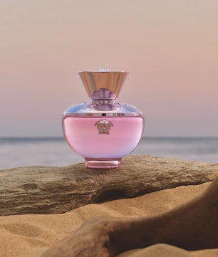 Pink perfume bottle on a log with a beach background