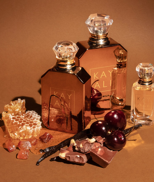 Perfume bottles with honeycomb, vanilla beans, and cherries on a brown background