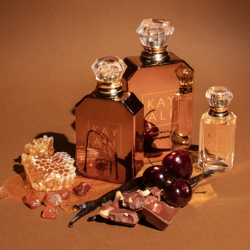 Perfume bottles with honeycomb, vanilla beans, and cherries on a brown background