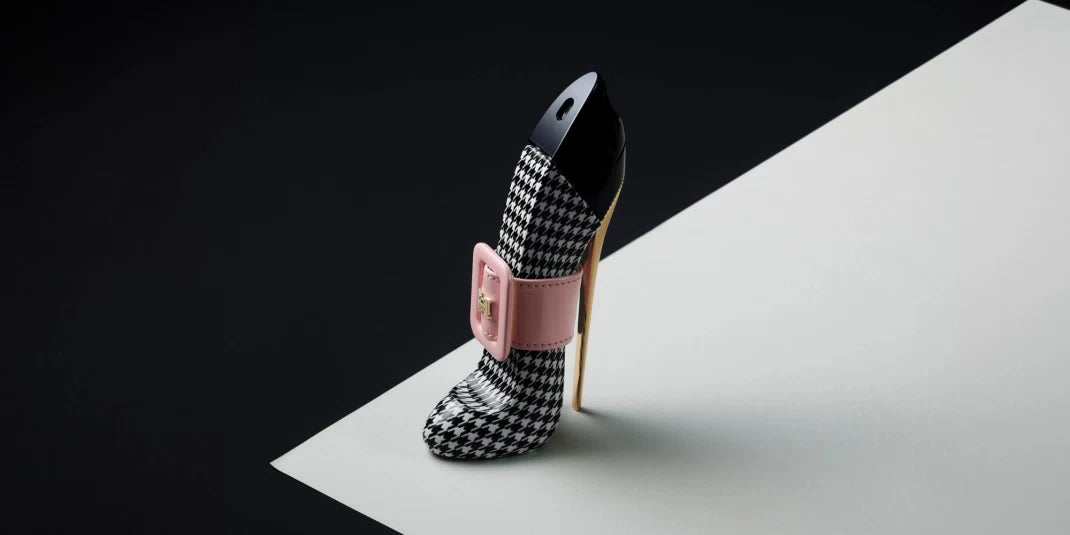 High-heeled shoe with houndstooth pattern and pink buckle on a white platform with black background