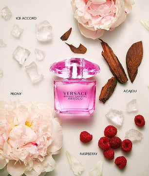 Pink Versace perfume bottle surrounded by flowers, berries, and ice on a light background