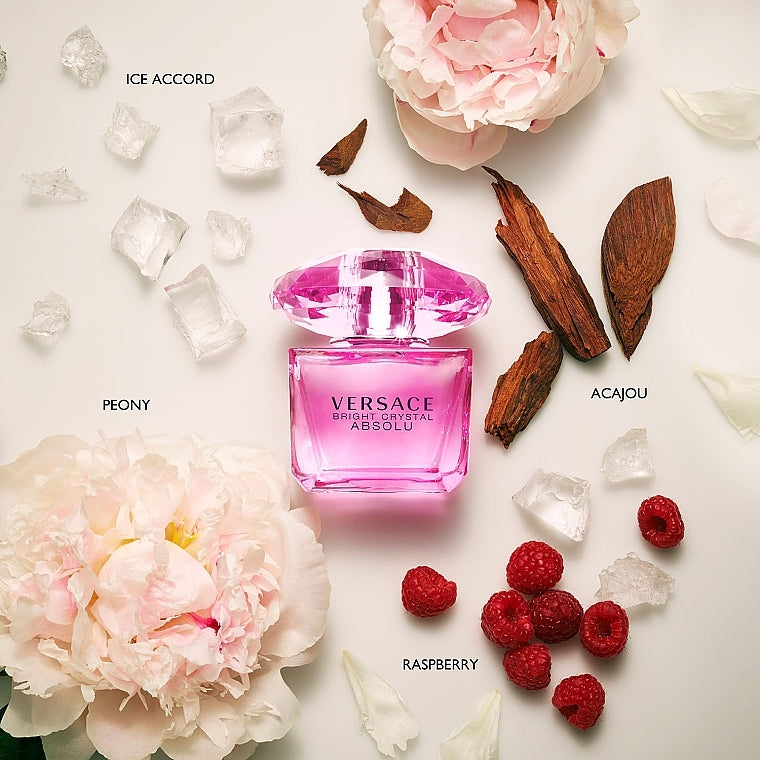 Pink Versace perfume bottle surrounded by flowers, berries, and ice on a light background