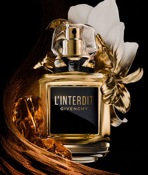 Givenchy L'Interdit perfume bottle with a gold and clear cap, a black label with gold lettering, and decorative gold leaves and white petals on a black background.