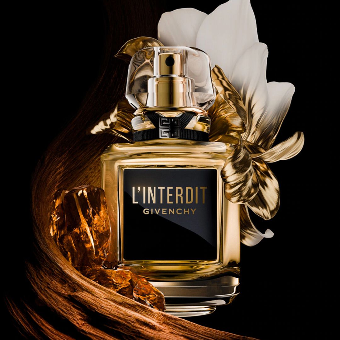 Givenchy L'Interdit perfume bottle with a gold and clear cap, a black label with gold lettering, and decorative gold leaves and white petals on a black background.