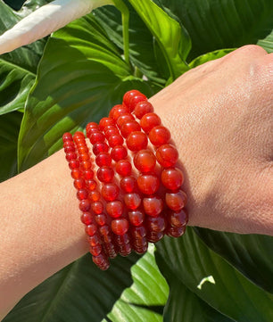 Red beaded bracelet on a wrist with green leaves in the background