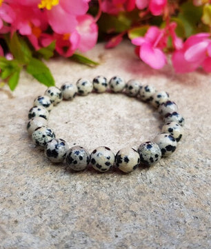 Bracelet with black and white beads on a stone surface with pink flowers in the background