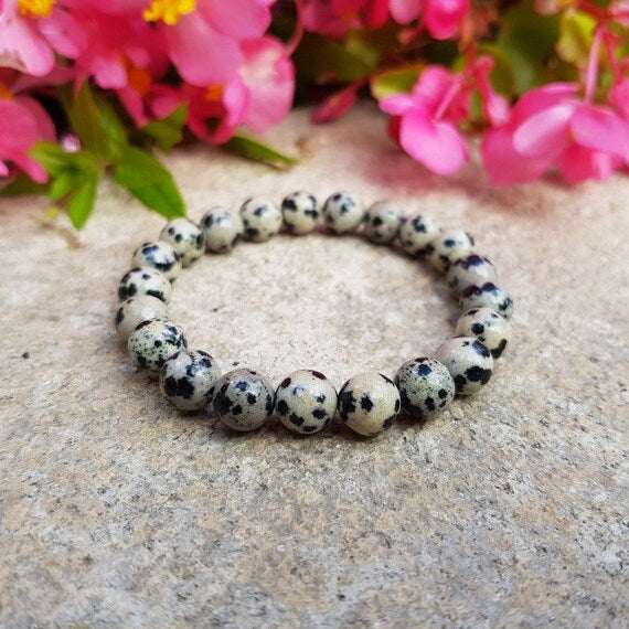 Bracelet with black and white beads on a stone surface with pink flowers in the background