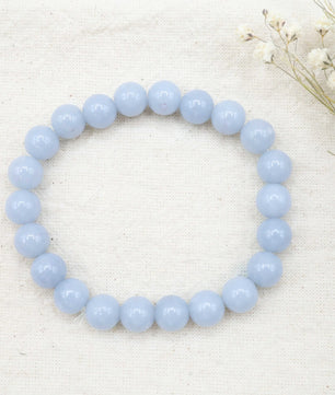 Light blue beaded bracelet on a white fabric background with dried flowers.