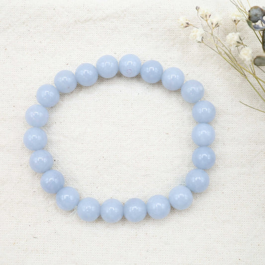 Light blue beaded bracelet on a white fabric background with dried flowers.