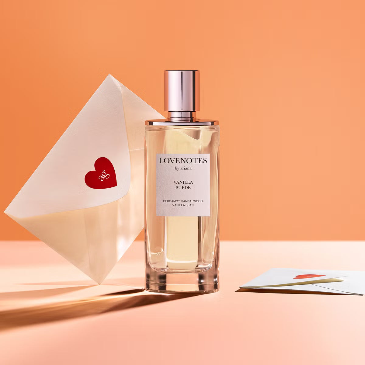 Perfume bottle labeled 'Lovenotes' with a heart-shaped card on an orange background