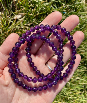 Purple beaded necklace held in a hand with grass in the background