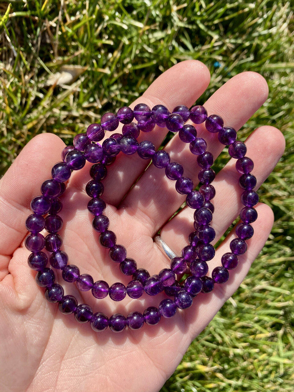 Purple beaded necklace held in a hand with grass in the background