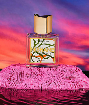 Perfume bottle with colorful label on a pink textured surface against a vibrant sunset sky