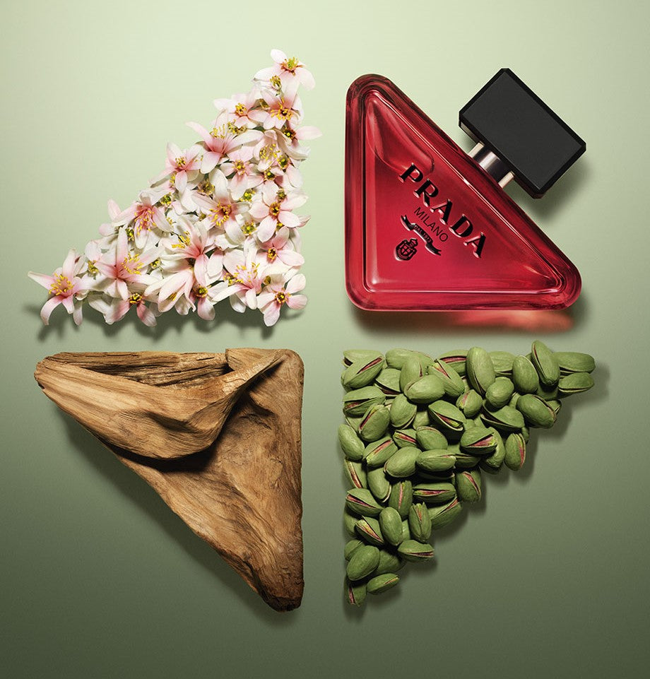 Prada perfume bottle with flowers, wooden leaf, and green seeds on a green background
