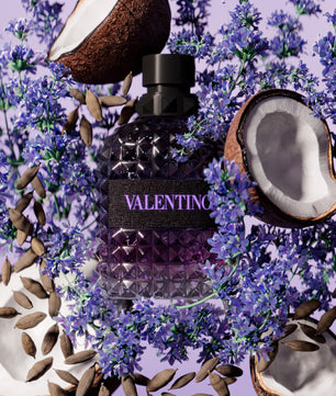 Valentino perfume bottle surrounded by coconut halves and lavender flowers on a purple background