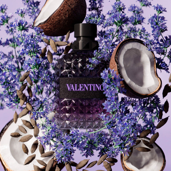 Valentino perfume bottle surrounded by coconut halves and lavender flowers on a purple background