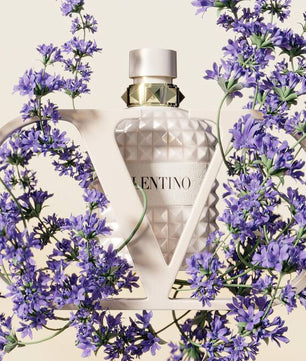 Fragrance bottle with geometric design surrounded by purple flowers on a light background